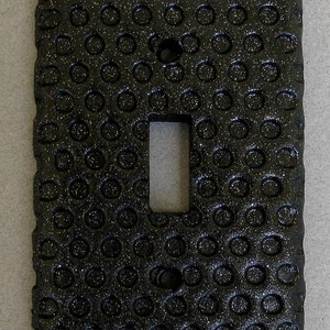 May include: Black light switch cover with a textured surface of small circles.