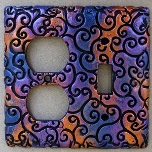 May include: A decorative outlet cover with a swirling pattern in shades of purple, blue, and copper. The cover has two outlets and a single switch.
