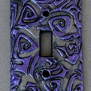 May include: A purple and silver light switch cover with a swirling, textured design.