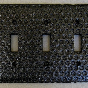 May include: Black triple light switch cover with a textured, dimpled surface.