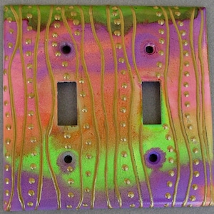 May include: A double light switch cover with a colorful abstract design. The cover features a wavy pattern in shades of pink, purple, green, and gold with gold dots.