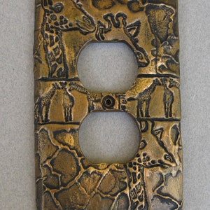 May include: A decorative outlet cover with a textured, bronze-colored finish. The cover features an embossed design of giraffes and a giraffe print pattern.
