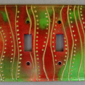 May include: A red and green light switch cover with a wavy pattern and gold accents. The cover has three toggle switches.