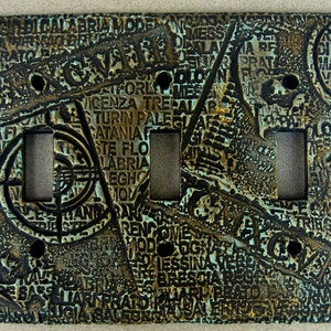 May include: A decorative light switch cover with a textured, metallic finish. The cover features a design of overlapping words and patterns in shades of brown, gold, and blue.