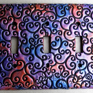 May include: A decorative light switch cover with a swirling pattern in shades of purple, blue, and red. The cover has three switch openings.