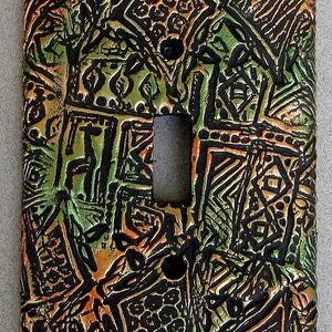May include: A decorative light switch cover with an abstract design in black, green, and orange. The design features geometric shapes and patterns.