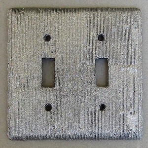 May include: A silver light switch cover with a textured surface and two toggle switches.