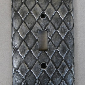 May include: A silver light switch cover with a diamond pattern. The cover is made of metal and has a textured surface.