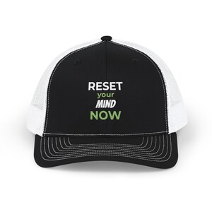Peut inclure: Une casquette de type trucker noire et blanche avec un panneau arrière en filet et un panneau avant solide. L'avant affiche le texte RESET your MIND NOW en lettres blanches et vert clair. La visière est courbée avec des coutures visibles.