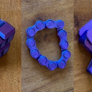 Könnte beinhalten: Drei Zappelspielzeuge in Blau- und Lilatönen liegen auf einer Holzoberfläche. Eines ist ein Würfel, ein anderes ein kettenartiger Ring, und das dritte ist ein segmentiertes, bewegliches Rechteck. Die Spielzeuge sind zum Manipulieren konzipiert.