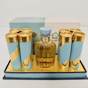 May include: A vintage Old Spice gift set featuring a central glass bottle of Toilet Water with a light blue cap, surrounded by six cylindrical containers of Bubbling Bath Crystals. The containers are light blue with gold diagonal stripes.