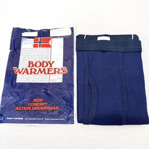 May include: Navy blue boxer briefs with a dark elastic waistband, next to a package of "Body Warmers" underwear. The package is dark blue with white text and a flag design. The text "New Concept Action Underwear" is also visible.