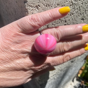 May include: A pink and white ring with a swirl design. The ring is made of resin and is a statement piece.