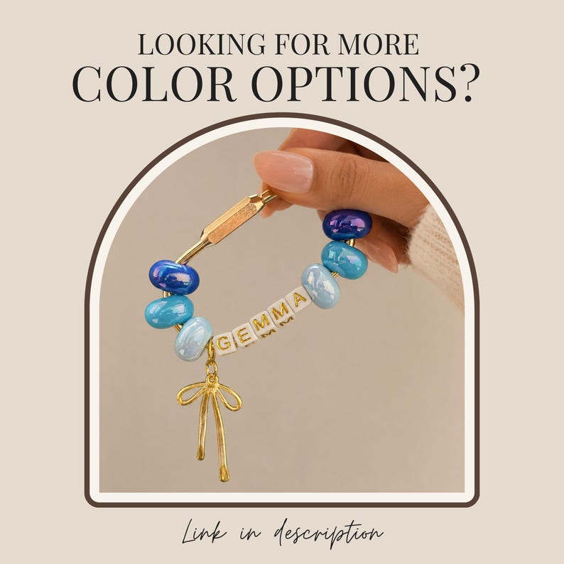 May include: A gold-toned carabiner keychain featuring blue and light blue glass beads, white letter beads spelling the name GEMMA, and a gold-toned bow charm. The text LOOKING FOR MORE COLOR OPTIONS? and Link in description are visible.