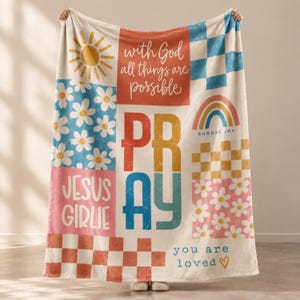 May include: A soft throw blanket featuring a patchwork design with various motifs including a yellow sun, blue and pink daisy patterns, checkered squares, a rainbow, and the text "with God all things are possible", "PRAY", "JESUS GIRLIE", and "you are loved".