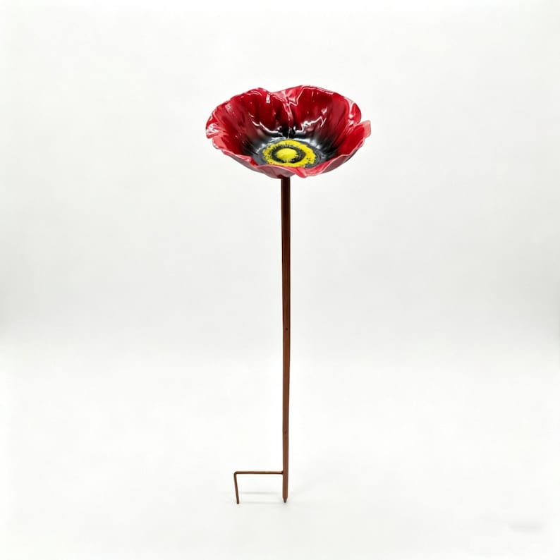 May include: A red poppy garden stake with a black center and yellow accents. The flower is made of a shiny material and is mounted on a brown metal pole with a ground stake.