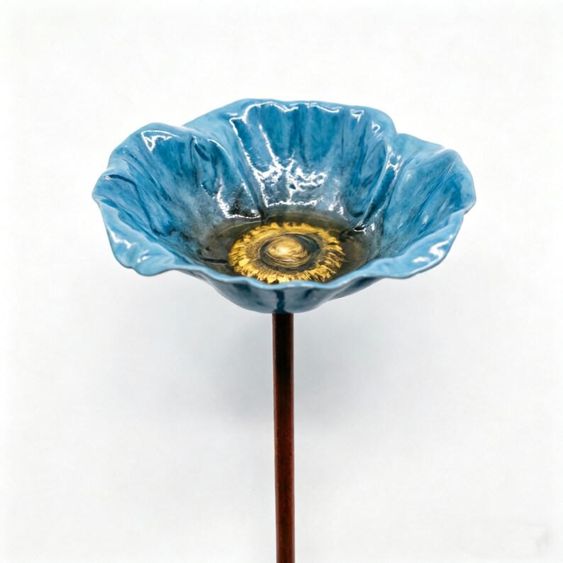 May include: A ceramic blue poppy flower with a golden center, mounted on a brown metal stem. The flower has a glossy finish and detailed petal edges. The poppy is a decorative garden accent.