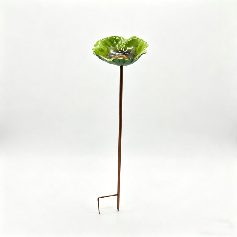 May include: A green ceramic bird bath with a flower-shaped bowl and a brown metal stake. The bowl has a glossy finish and a dark center. The stake has a ground anchor for easy placement in a garden or yard.