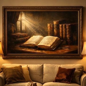 Puede incluir: Pintura enmarcada de un libro abierto iluminado por un rayo de luz, rodeado de otros libros. La obra de arte tiene una paleta de colores oscuros y cálidos, con un marco de madera detallado. Dos lámparas con pantallas beige flanquean un sofá beige con cojines.