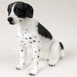 May include: A black and white figurine of a dog sitting. The dog has black ears, a black patch on its back, and white spots on its body.