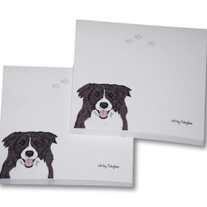 May include: Two white notepads with a black and white border collie illustration on each. The notepads have the text "art by Satyrlee" at the bottom.