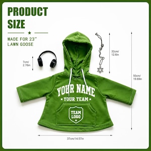 May include: A green hooded sweatshirt for a 23-inch lawn goose, featuring white text reading YOUR NAME, YOUR TEAM, and TEAM LOGO on a shield graphic. Includes black headphones and a silver Star of David pendant. Dimensions are 19.69 inches long.