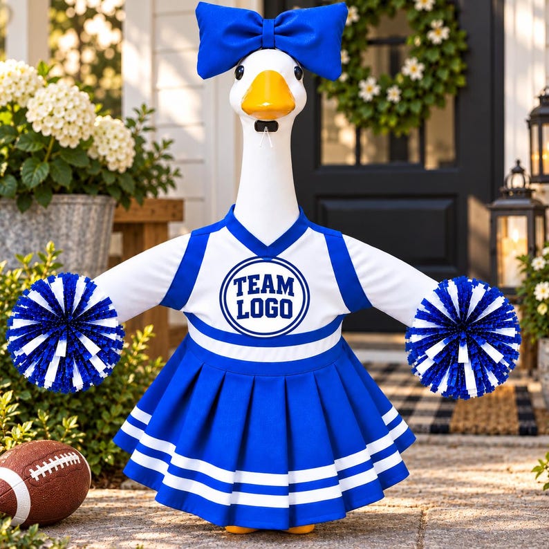 K&ouml;nnte beinhalten: Eine wei&szlig;e G&auml;nsefigur in einem blau-wei&szlig;en Cheerleader-Outfit mit einer passenden blauen Schleife auf dem Kopf. Das Outfit besteht aus einem Oberteil mit V-Ausschnitt, dem Text "TEAM LOGO" in einem Kreis und einem Faltenrock. Sie h&auml;lt Pompons.