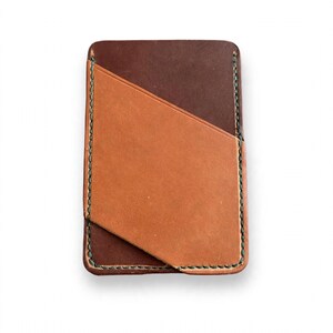 May include: A rectangular leather card holder featuring a dark brown base layer and a lighter tan diagonal pocket overlay. The edges are secured with visible dark green stitching, creating a clean, structured design for holding cards.