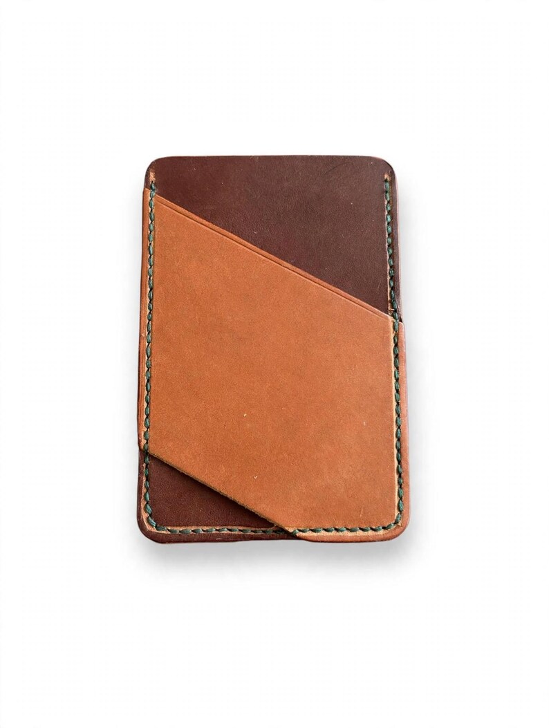 May include: A rectangular leather card holder featuring a dark brown base layer and a lighter tan diagonal pocket overlay. The edges are secured with visible dark green stitching, creating a clean, structured design for holding cards.