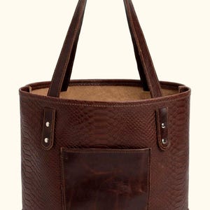 May include: A dark brown leather tote bag featuring a snakeskin-embossed texture on the main body, a smooth leather exterior pocket, two vertical strap attachments secured with silver-toned metal rivets, and two long shoulder straps.