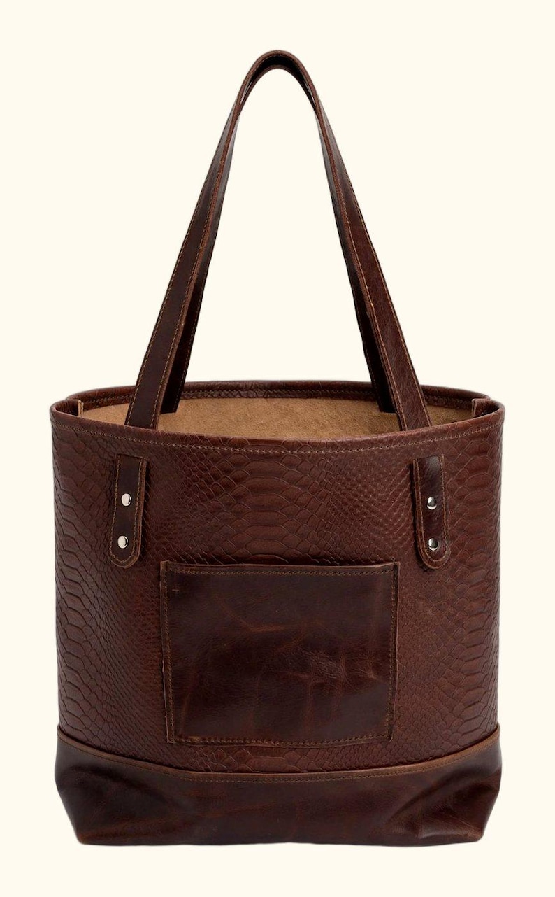 May include: A dark brown leather tote bag featuring a snakeskin-embossed texture on the main body, a smooth leather exterior pocket, two vertical strap attachments secured with silver-toned metal rivets, and two long shoulder straps.