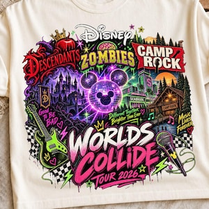 Pode incluir: Uma t-shirt de cor creme com uma impressão gráfica vibrante com o texto Disney, Descendants, Zombies, Camp Rock e Worlds Collide Tour 2026. O design inclui um ícone do Mickey Mouse tipo bola de discoteca, uma guitarra elétrica verde e um microfone.