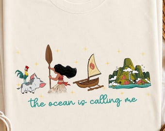 May include: A cream-colored t-shirt featuring a graphic print of a rooster, a pig, a person holding a wooden paddle, a small sailboat, and a tropical island. Below the illustrations, the text reads, the ocean is calling me, in teal.