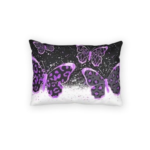 Peut inclure: Coussin rectangulaire avec un fond noir et un motif de papillons violets. Les papillons ont un motif léopard gris et violet. Des mouchetures blanches sont dispersées sur le fond noir.