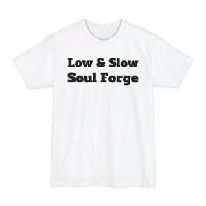 Pode incluir: Camiseta branca com o texto "Low & Slow Soul Forge" impresso em letras pretas e em negrito. A camiseta tem gola redonda e mangas curtas. O design está centralizado na frente da camiseta.