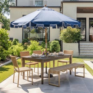 May include: Outdoor dining set with a navy blue and white scalloped umbrella, a wooden table, woven chairs, and a bench. The table is set with plates and flowers, creating an inviting patio scene.