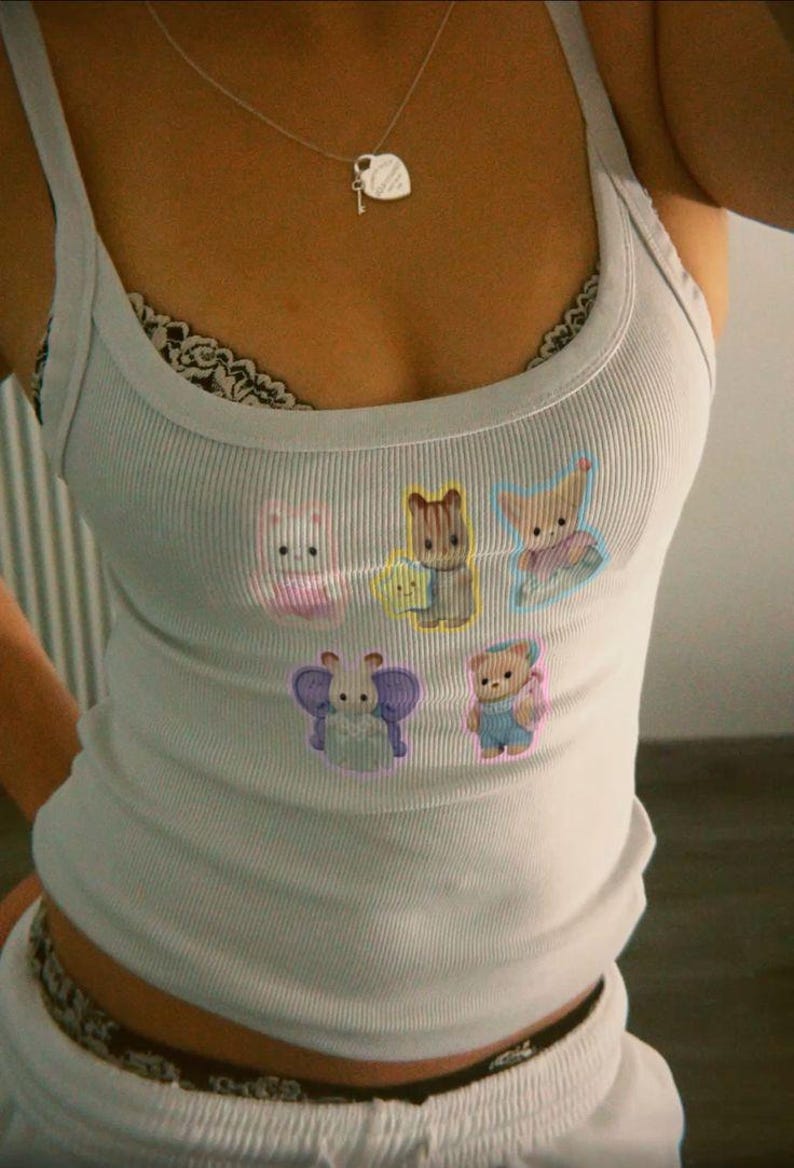 May include: A light blue ribbed tank top with cartoon animal graphics. The tank top has a scoop neckline and thin straps. A silver necklace with a heart-shaped pendant is visible. The top is paired with white bottoms.