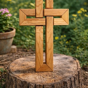 Könnte beinhalten: Ein Holzkreuz mit einem einzigartigen, ineinandergreifenden Design. Das Kreuz besteht aus hellbraunem Holz und steht auf einem Baumstumpf. Der Hintergrund zeigt grünes Laub und einen verschwommenen Garten.
