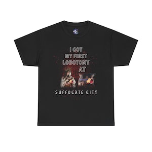 Pode incluir: T-shirt preta com o texto "I GOT MY FIRST LOBOTOMY AT SUFFOCATE CITY" em branco e vermelho. A camisa apresenta um gráfico de duas figuras. A t-shirt é feita de um material macio e confortável.