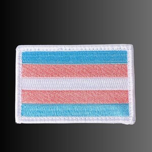 May include: A rectangular embroidered patch featuring five horizontal stripes in a specific color sequence. The top and bottom stripes are light blue, followed by two inner stripes of light pink, and a central white stripe with a white border.