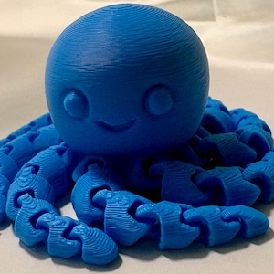May include: A bright blue 3D printed octopus figurine with a large rounded head, two circular eyes, and a small curved mouth. The creature features multiple articulated, segmented tentacles that extend outward from the central body base.