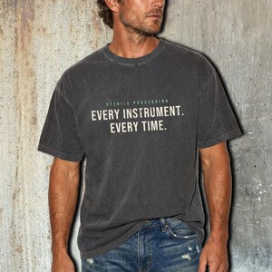May include: A charcoal grey short-sleeve t-shirt featuring the text STERILE PROCESSING EVERY INSTRUMENT. EVERY TIME. printed in a light beige color across the chest. The shirt has a crew neckline and a slightly faded, washed-out fabric appearance.