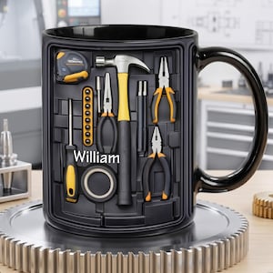 May include: Black ceramic mug featuring a toolbox design with various tools, including a hammer, pliers, and measuring tape. The name "William" is printed on the mug. The mug is sitting on a metal gear.