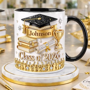 Peut inclure: Tasse en céramique blanche avec une anse et un bord noirs, sur le thème de la remise de diplômes. Le design comprend une toque, des livres, un trophée et un parchemin, avec le nom "Johnson" et "Class of 2026" en or et cristaux.