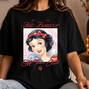 May include: A black t-shirt featuring a graphic of a character with black hair and a red bow, a red apple, and the text "EST 1937 THE FAIREST Off Them All" in red lettering. A small red skull icon is printed below the main graphic design.