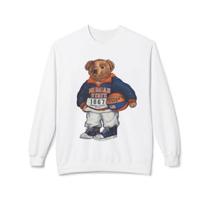 May include: White sweatshirt featuring a cartoon bear wearing a blue and orange jacket and holding a basketball. The jacket and basketball display "MORGAN STATE" and "1867" text. The bear is wearing white pants and blue sneakers.
