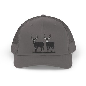 Peut inclure: Casquette de camionneur grise avec une silhouette noire de deux cerfs avec des bois sur de l'herbe. La casquette a un dos en filet et une visière incurvée. Le motif des cerfs est centré sur le devant.