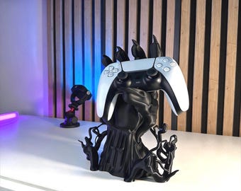 May include: A black 3D printed controller stand shaped like a clawed hand with vine-like roots at the base, holding a white and black video game controller. The text 3D FACTORY BOX is visible in the upper left corner of the image.