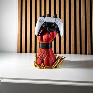 May include: A red sculpted hand with a black wrist cuff holding a white and black video game controller. The base of the hand is surrounded by several gold-colored bullet casings. The hand features textured details and claw-like markings.