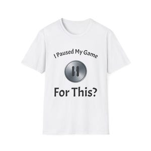 May include: White t-shirt with the text "I Paused My Game For This?" above a silver pause button graphic. The shirt is a crew neck style and appears to be made of a soft material.
